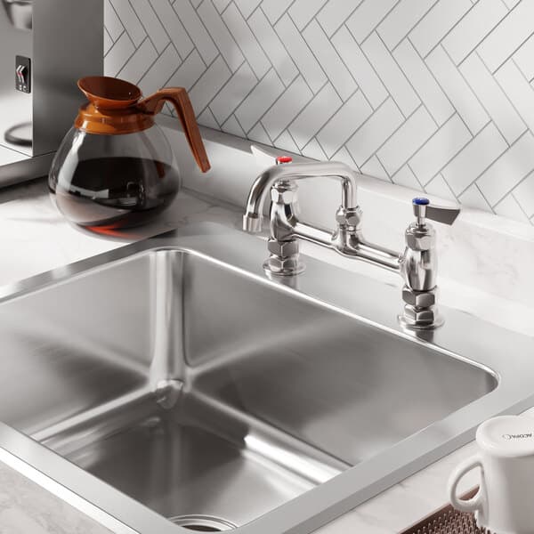 A stainless steel deck-mounted faucet with 8-inch centers and a 6-inch swing spout installed on a kitchen sink.