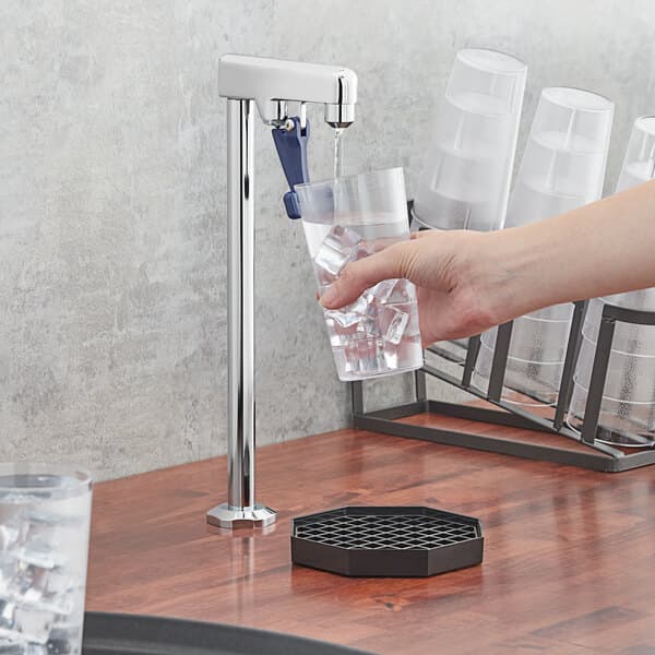 A person using a Waterloo countertop glass filler to pour water into a glass on a counter.