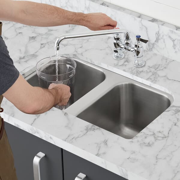 A person filling a glass with water from a stainless steel Waterloo undermount sink.