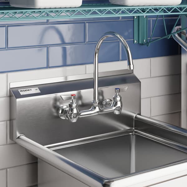 A wall-mounted stainless steel faucet with an 8-inch gooseneck spout and dual handles, installed above a commercial sink.