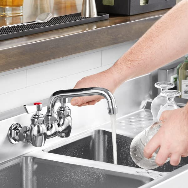 A person using a Waterloo wall-mounted faucet to pour water into a sink.