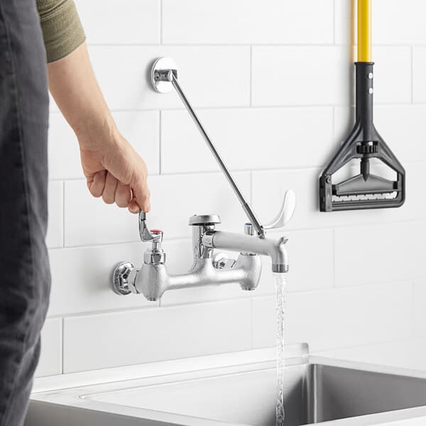 A person using a Waterloo wall-mounted mop sink faucet with wrist blade handles to open a sink.