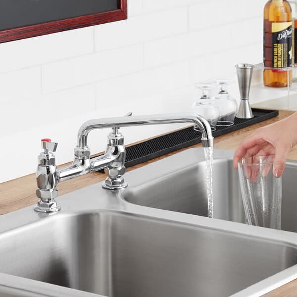 A woman using a Waterloo deck-mounted faucet to pour water into a glass over a metal sink.