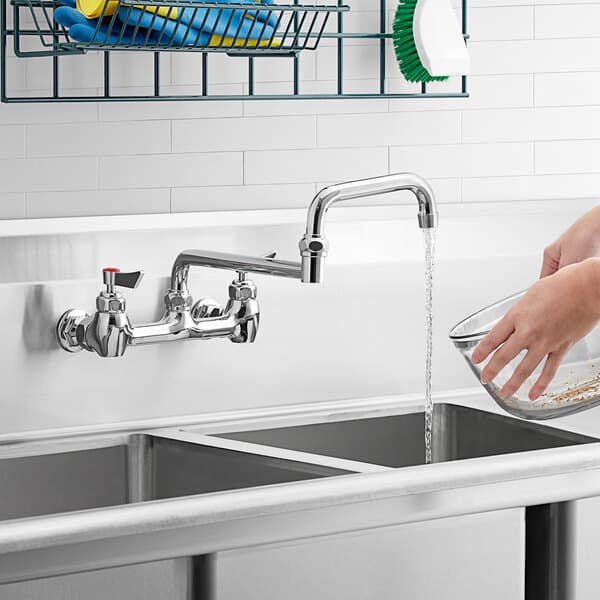 A hand washing a bowl in a sink using a Waterloo wall-mounted faucet.