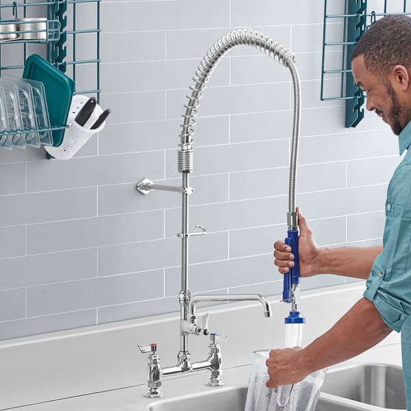 A man using a Waterloo pre-rinse faucet hose with handle to wash his hands in a kitchen sink.