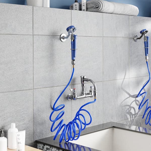 A Waterloo wall-mounted pet grooming faucet above a sink with blue hoses.
