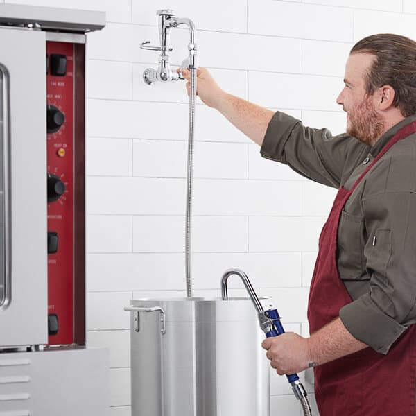 A man in an apron using a Waterloo wall-mounted pot and kettle filler hose.