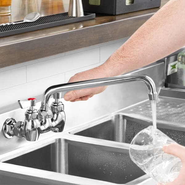 A person using a Waterloo wall-mounted faucet to pour water into a sink.
