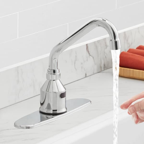 A hand using a Waterloo deck mount sensor faucet with a gooseneck spout over a sink.